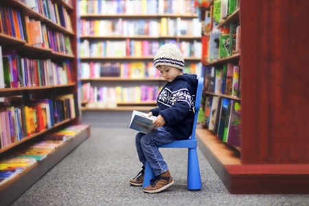 Child sitting on a chair in a library aisle